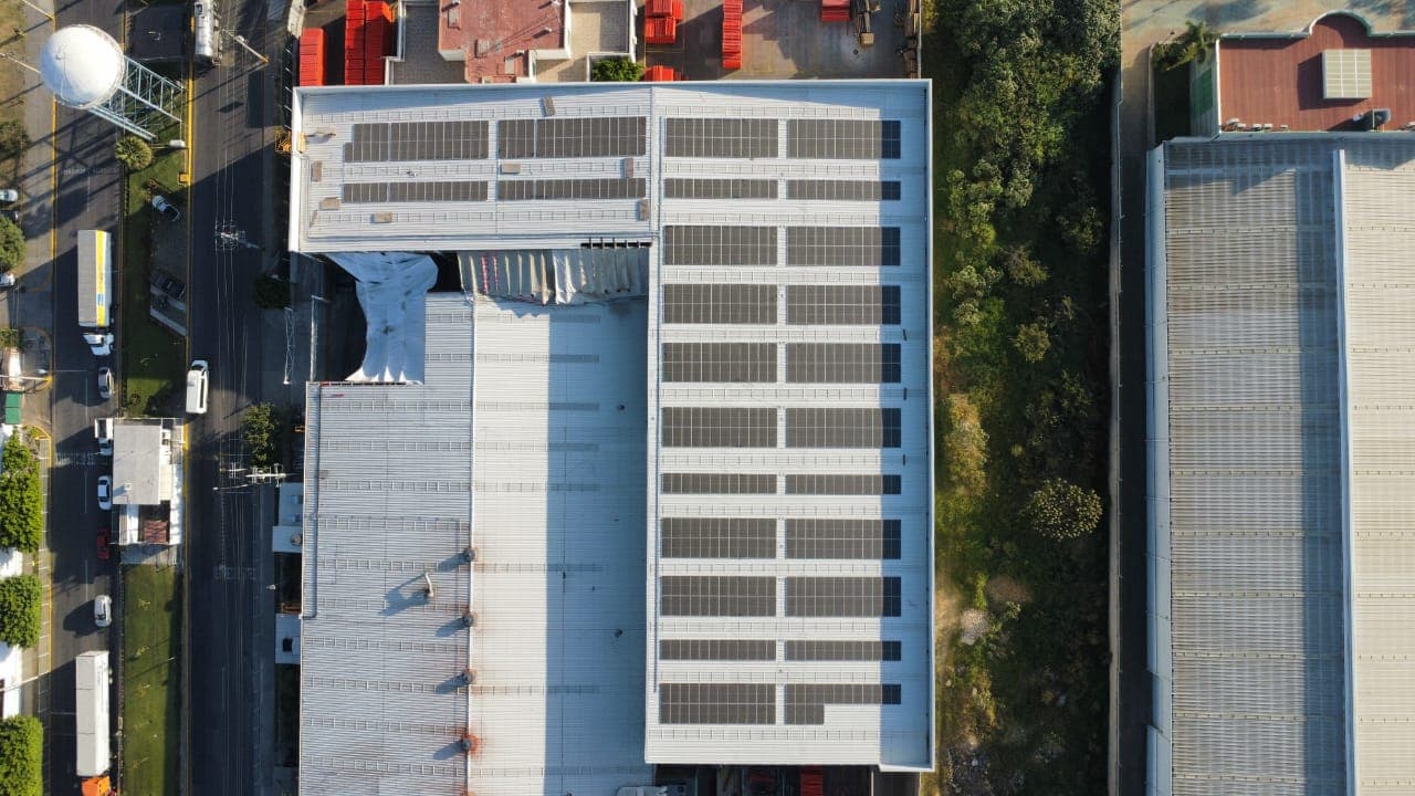 Vista aérea de un edificio industrial con paneles solares instalados en su techo blanco.