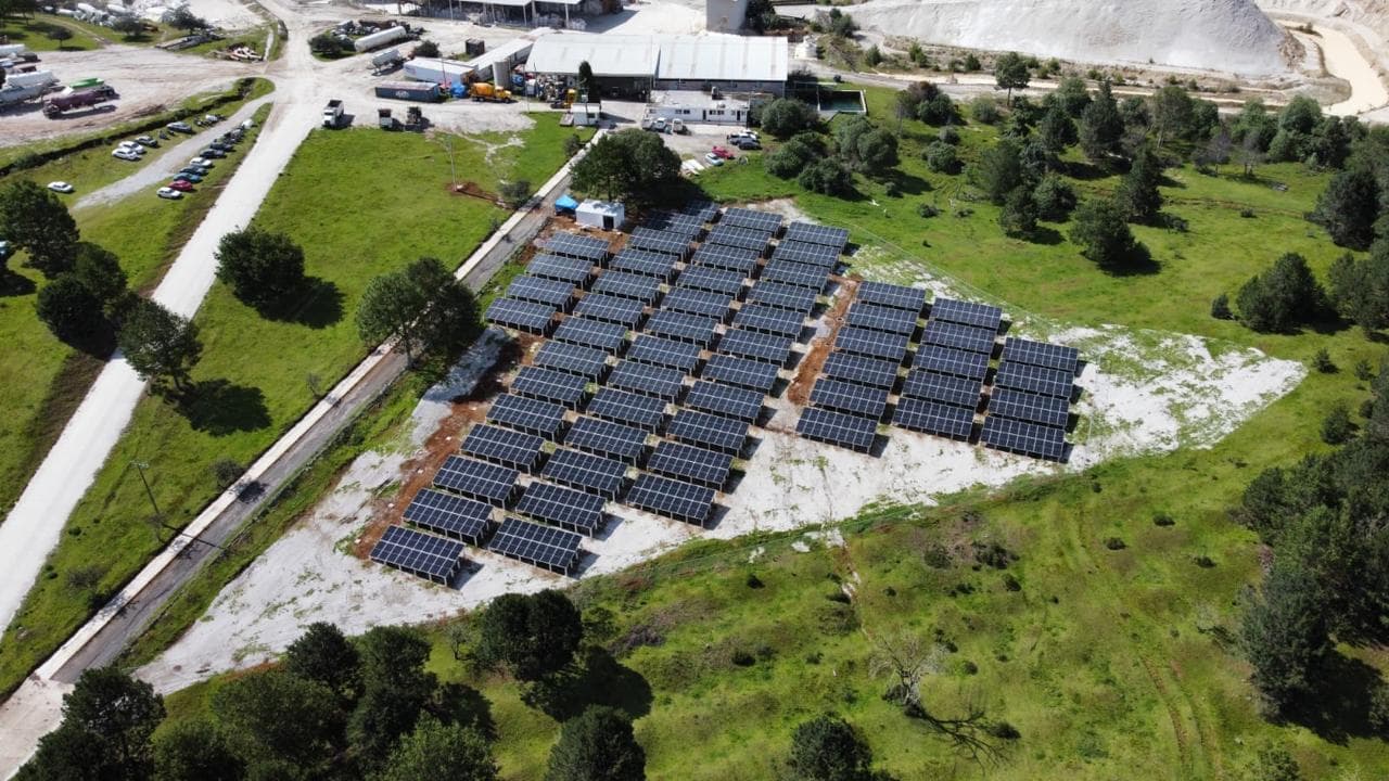 Vista aérea de paneles solares en filas sobre terreno despejado cerca de instalaciones industriales.