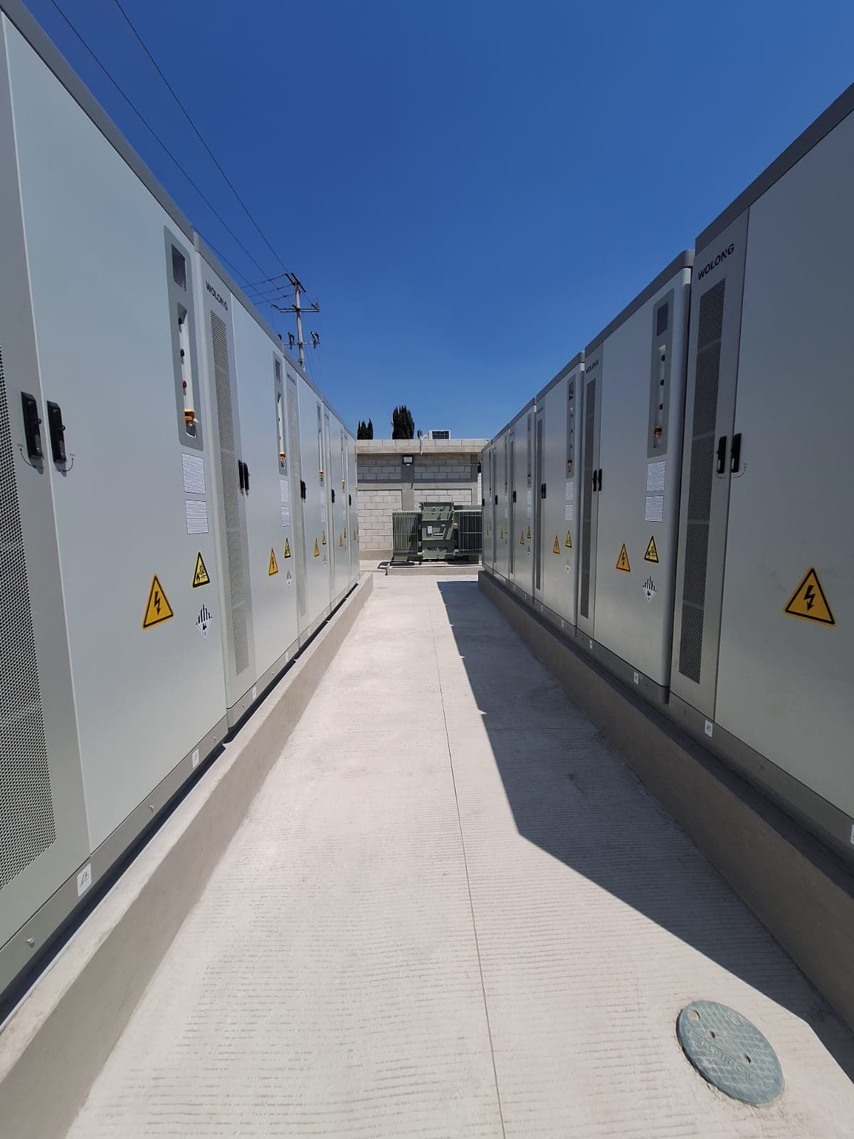 Filas de gabinetes eléctricos industriales con señales de alto voltaje bajo un cielo azul despejado.
