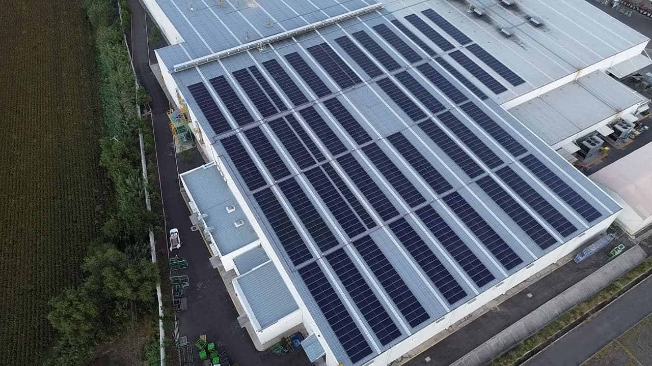 Vista aérea de filas de paneles solares instalados sobre el techo de un edificio industrial.